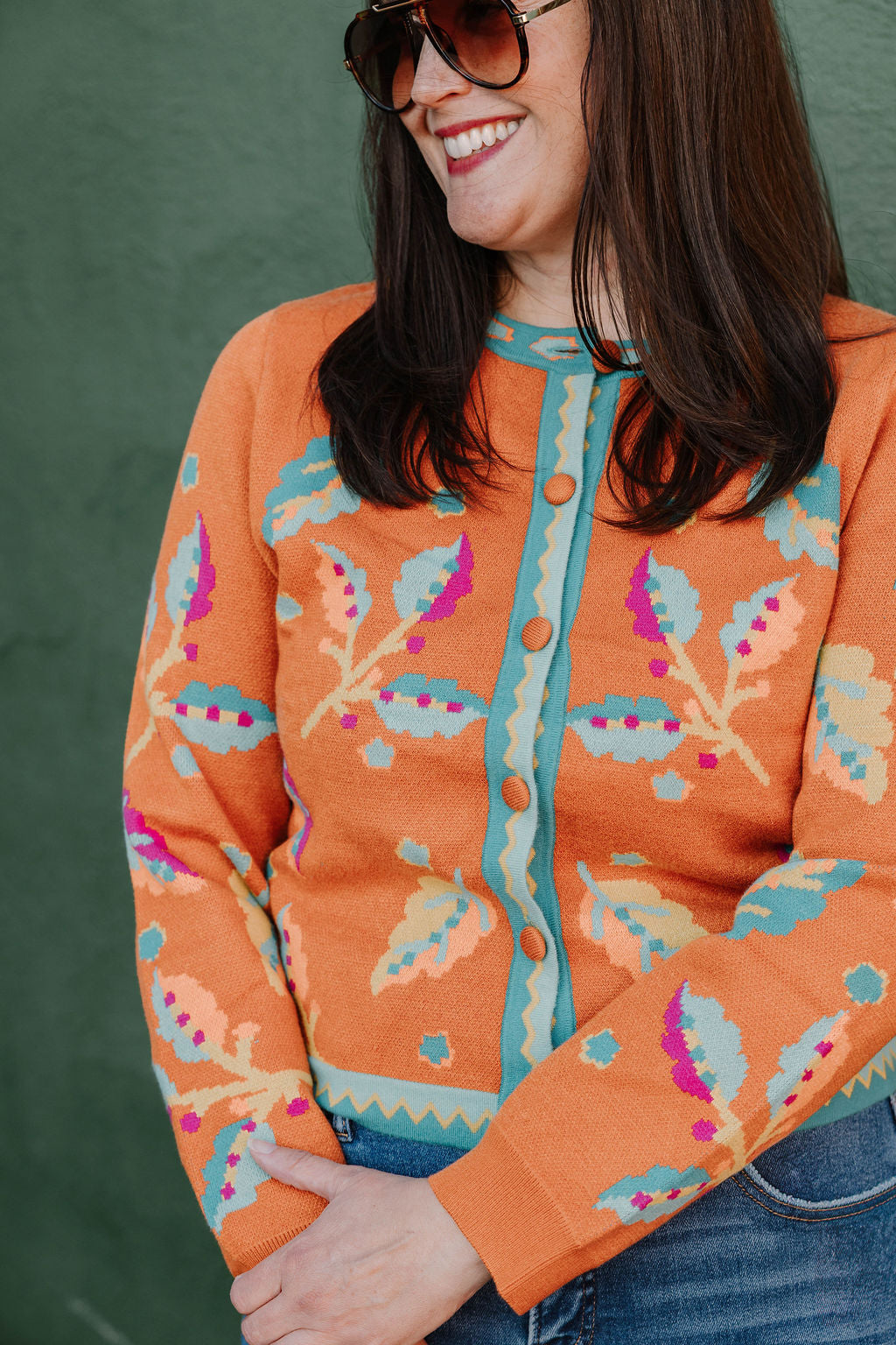bright orange cardigan with a colorful floral pattern in pink, teal, and mustard yellow with orange fabric covered buttons and teal trim